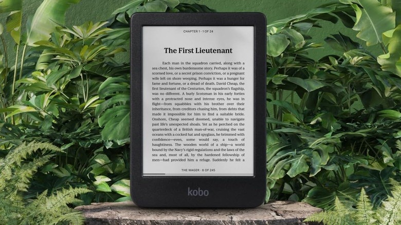 The Kobo Clara BW e-reader sitting on a grey stone surface with green plants in the background.