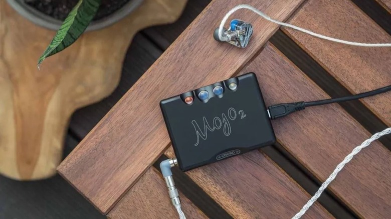 Chord Electronics Mojo 2 resting on a wood table with high-end in-ear monitors plugged in.