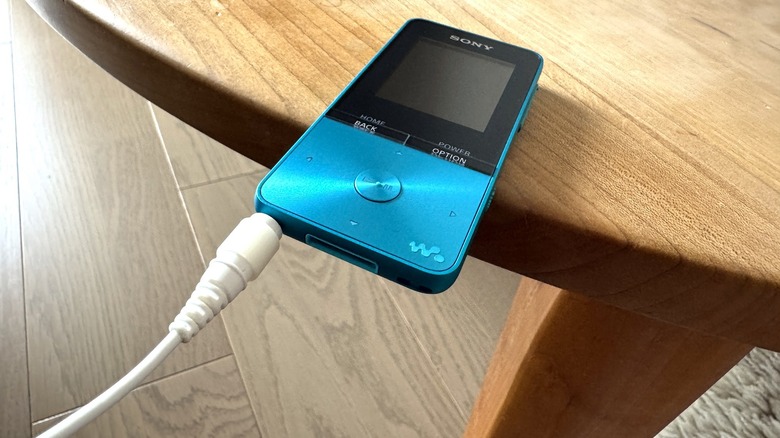 Wired earbuds connected to a music player that is sliding off the edge of a wooden table.