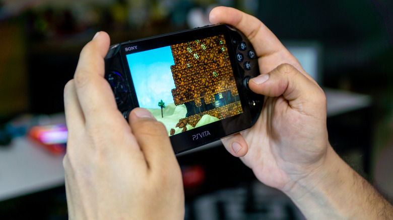 Hands holding a PlayStation Vita while playing the game Spelunky.