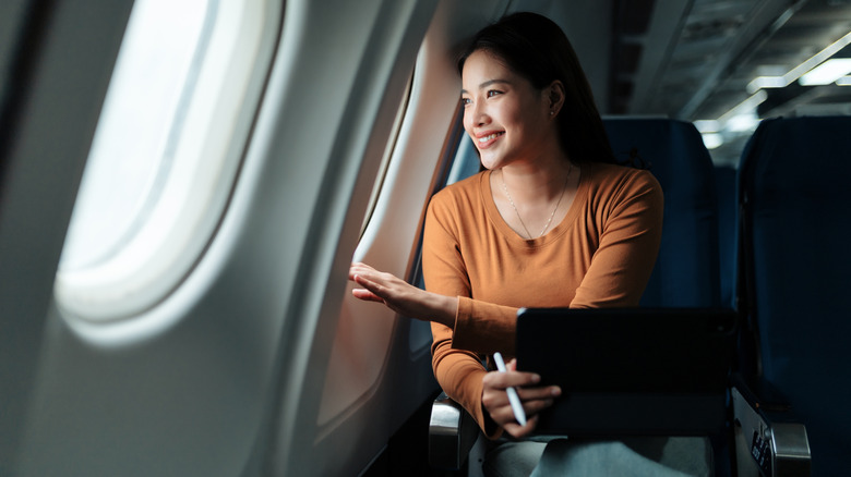 A woman looking out of an airplane window during a flight at sunset.