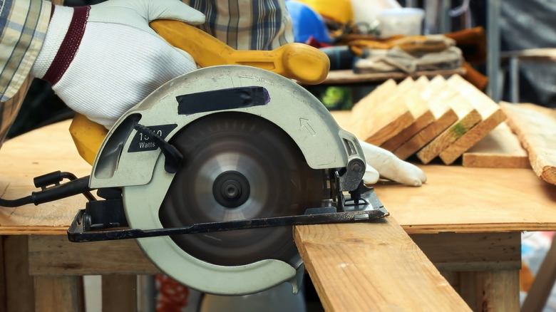 Close-up of a carpenter guiding a circular saw through a piece of lumber freehand.