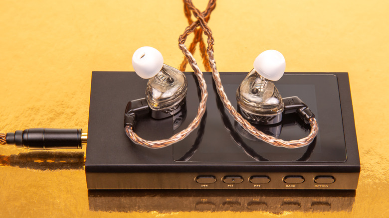 A portable DAC unit on a bright yellow background with in-ear monitors resting on top.