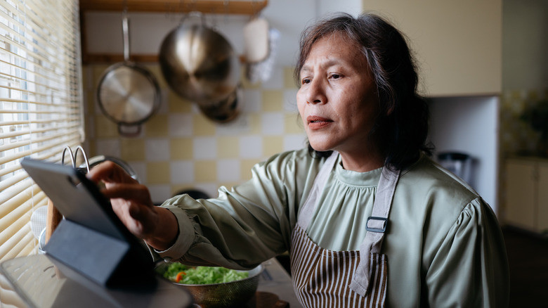 A person interacting with a screen on a kitchen countertop while cooking.