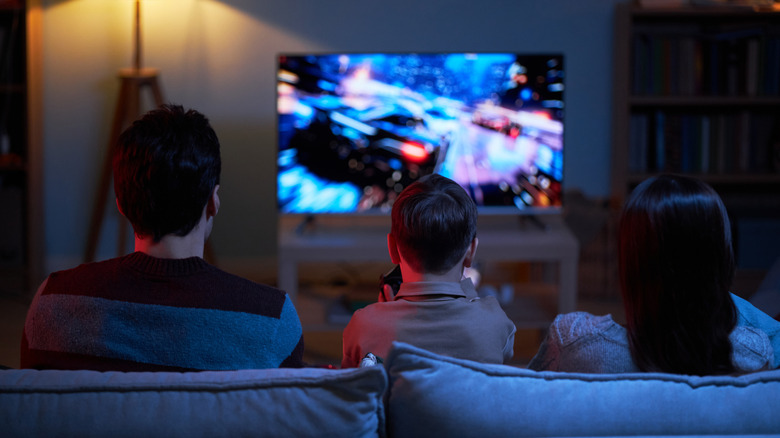 A family laughing and playing a video game together on a large flat-screen TV.