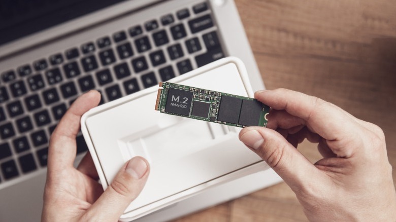 Close-up of a person holding a small M.2 NVMe SSD between their thumb and forefinger.