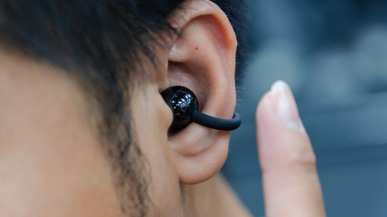 A close-up of a person wearing an ergonomic open-ear clip-on earbud designed for ambient transparency.
