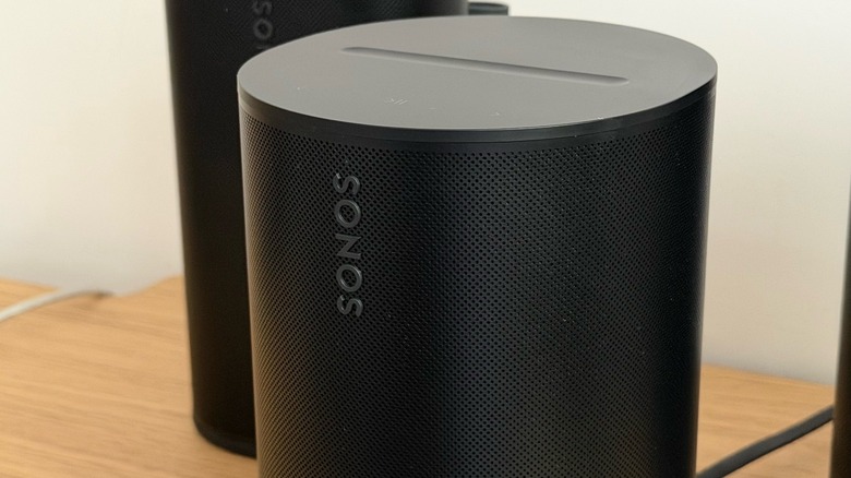 The Sonos Era 100 SL speaker positioned on a wooden table.