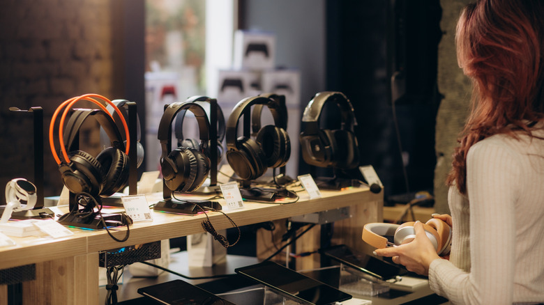 A woman examining a pair of headphones in a store setting.
