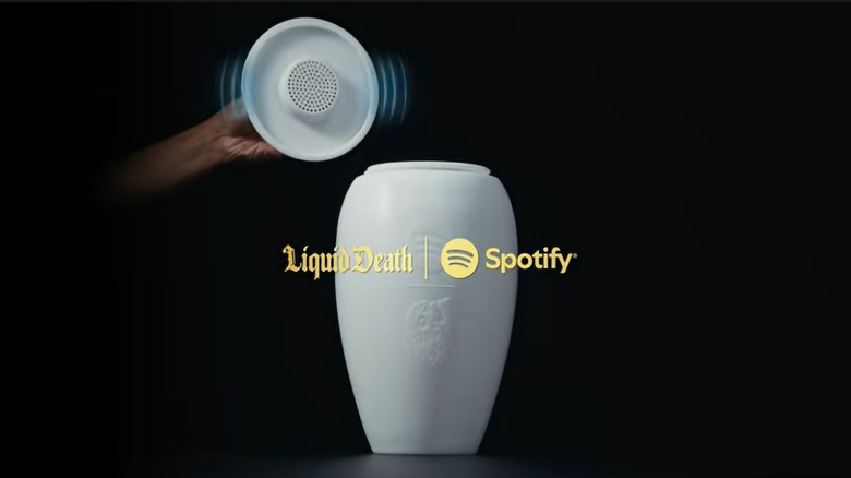 A close-up view of the Liquid Death urn lid being lifted to reveal the built-in Bluetooth speaker and internal branding.