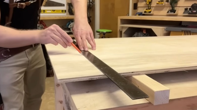 A person using a pencil to mark a precise cutting line on a wooden board.