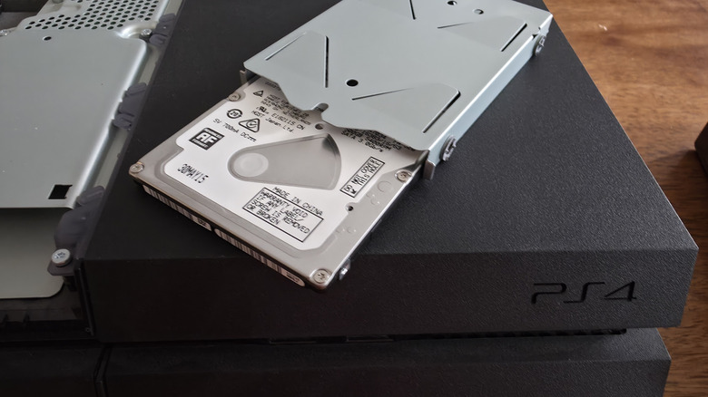 A standard mechanical hard drive being removed from its internal housing in a PlayStation 4.