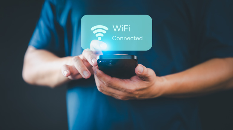 A close-up of a hand holding a phone with a digital Wi-Fi icon floating above it.