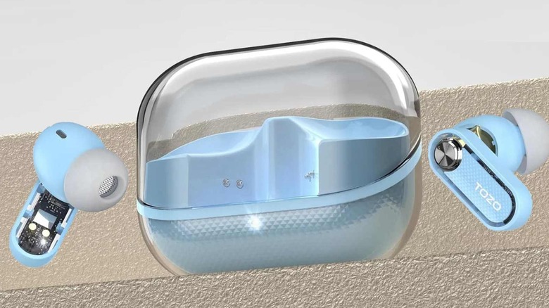 Light blue Tozo earbuds resting next to their translucent carrying case on a minimalist ledge.