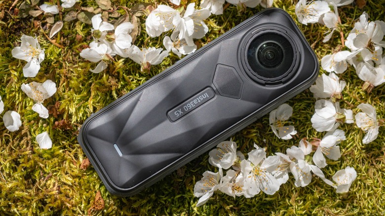 The Insta360 X5 placed on a bed of green moss and pink flower petals.