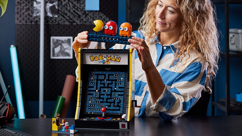 A person assembling the yellow LEGO Icons Pac-Man arcade cabinet set.