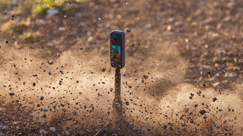 An Insta360 X5 camera standing on a tripod in a dusty, debris-filled environment.