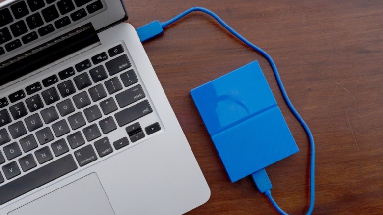 A portable external hard drive connected to a laptop port via a USB cable.