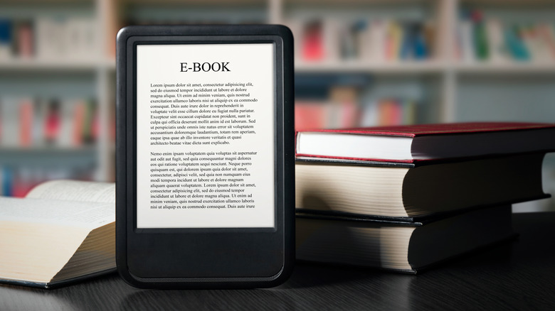 An e-reader resting on a library desk surrounded by bookshelves.