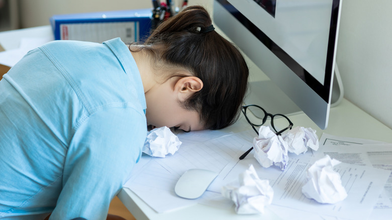 A woman with her head down on a desk surrounded by messy papers, symbolizing cognitive overload.