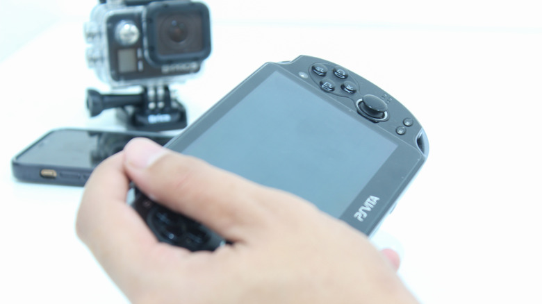 A close-up of a person holding a black PlayStation Vita handheld against a clean white background.