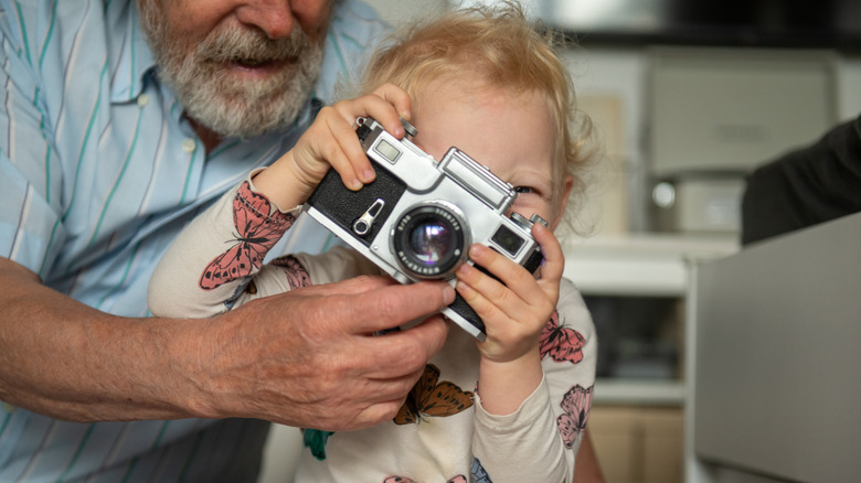 A close-up of a child focused on looking through the optical viewfinder of a camera.