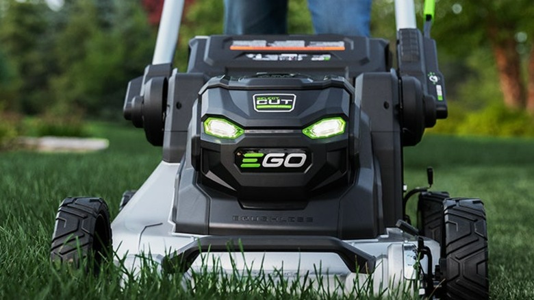 A green and black Ego lawn mower being pushed across a grass field.