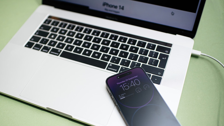An iPhone connected to a MacBook via a USB-C to Lightning cable for charging.