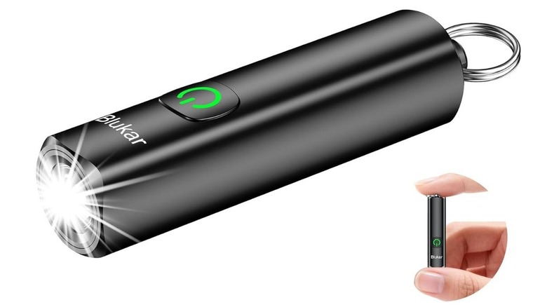 A hand holding the small black Blukar LED flashlight between two fingers to show its compact size.