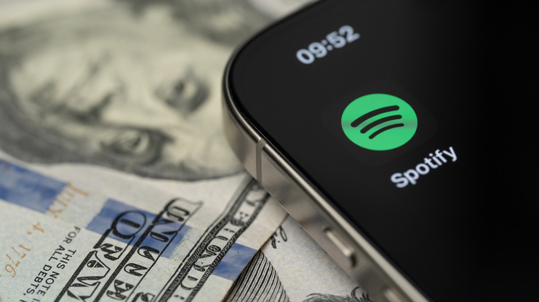 A smartphone showing the Spotify logo placed directly on top of a US one-hundred-dollar bill.