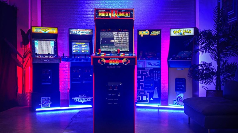 The Arcade1Up Mortal Kombat II Deluxe arcade machine standing prominently among other lit cabinets.