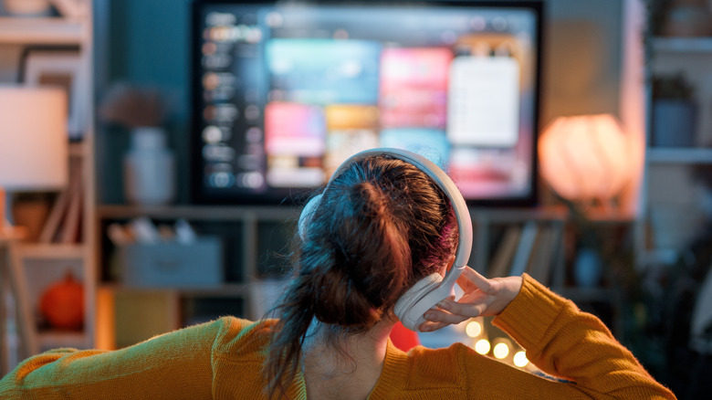 A person wearing over-ear white headphones while watching a bright television screen at night.