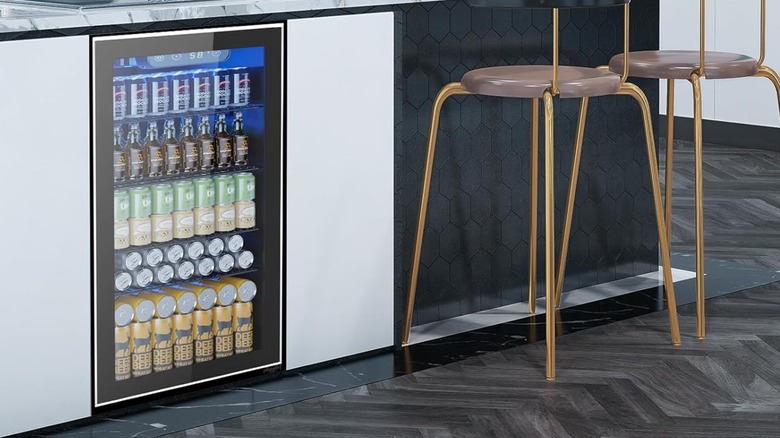 A sleek black beverage fridge stocked with cans installed under a counter next to gold barstools.