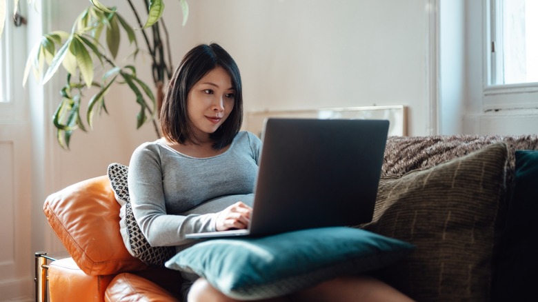 A woman smiling and working efficiently on her laptop in a bright, modern office space.
