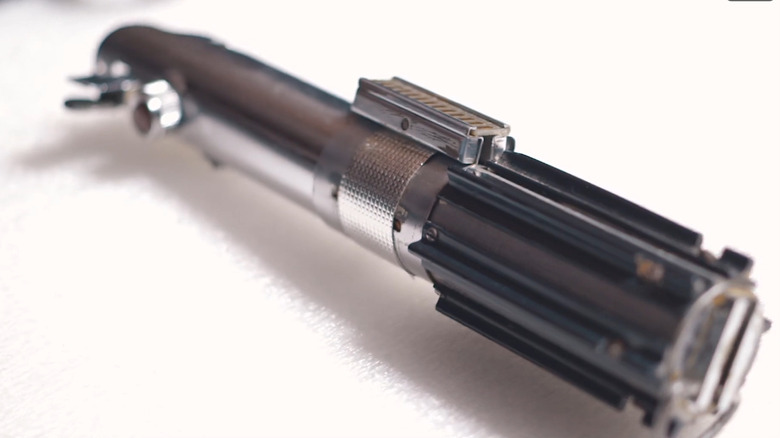 A close-up of the original lightsaber prop from A New Hope showing the chrome finish and clamp details.