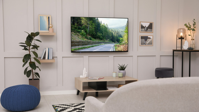 A sleek 4K television mounted on a white wall in a modern living room displaying a vibrant landscape.