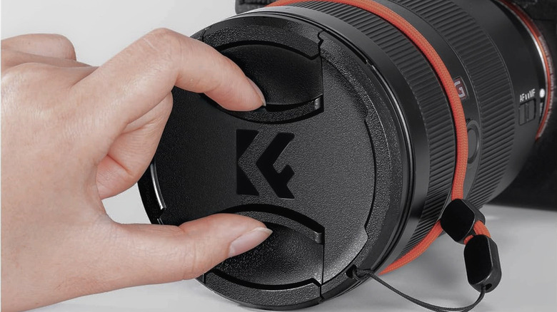 A hand pinching a K&F Concept professional lens cap to remove or attach it.