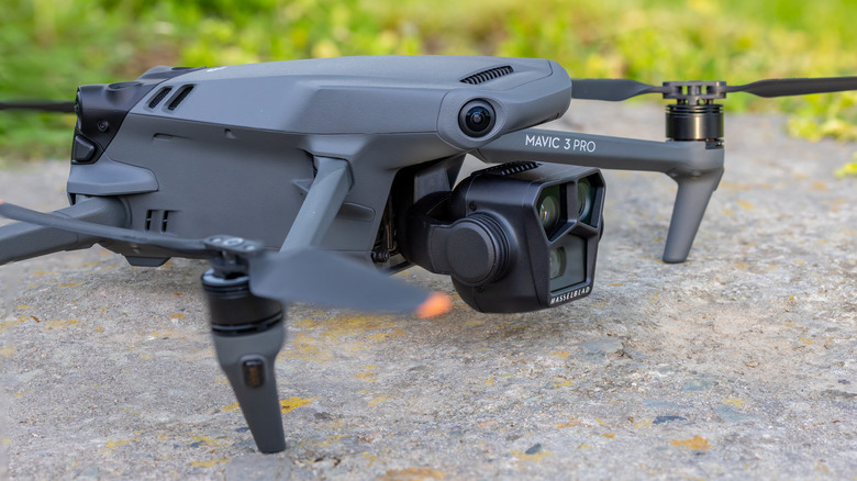 A modern DJI Mavic 3 Pro drone with its triple-camera system resting on a natural surface.