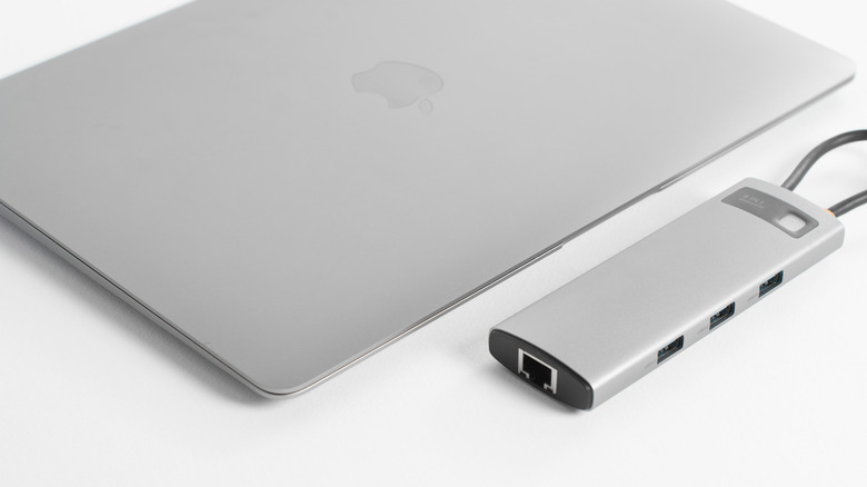 A closed MacBook connected to a multi-port USB-C hub on a clean desk.