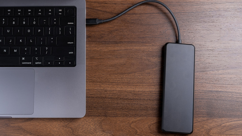 A slim external storage drive connected by cable to a laptop on a wooden surface.