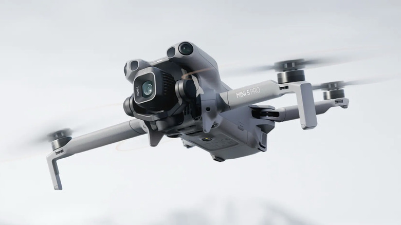 A DJI Mini series drone hovering stably in mid-air against a bright sky.