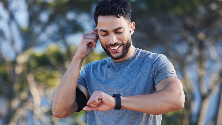 A person using a smartwatch to manage audio playback while wearing wireless earbuds.