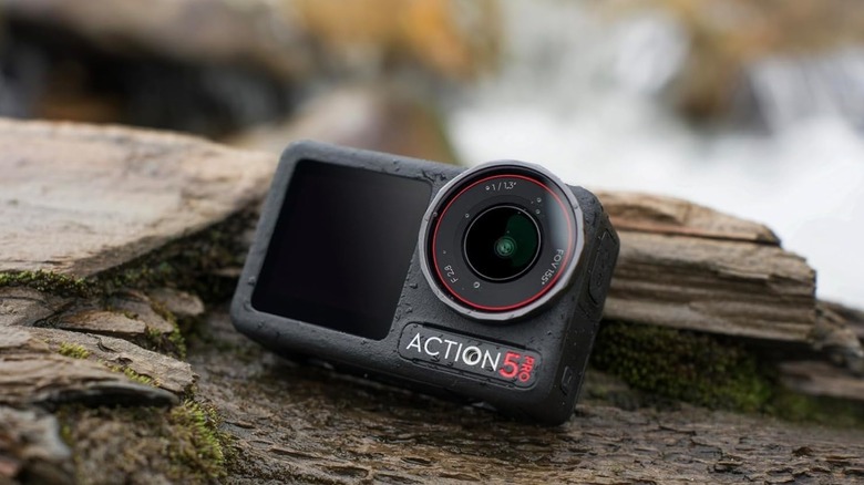 The DJI Osmo Action 5 Pro action camera shown splashed with water in a rugged outdoor setting.