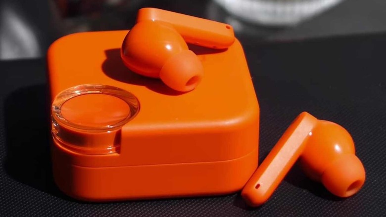 The vibrant orange CMF Buds 2 on a textured black surface showing the distinct case and earbud design.