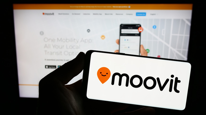 A hand holding an iPhone displaying the Moovit logo.