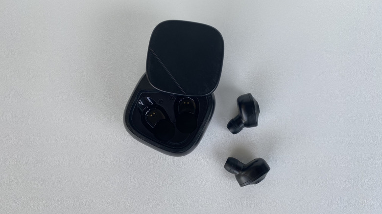 Black wireless earbuds and their matching charging case on a neutral surface.