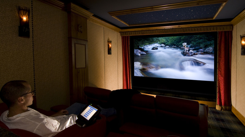 A viewer sitting in a darkened home theater room being immersed by a movie.