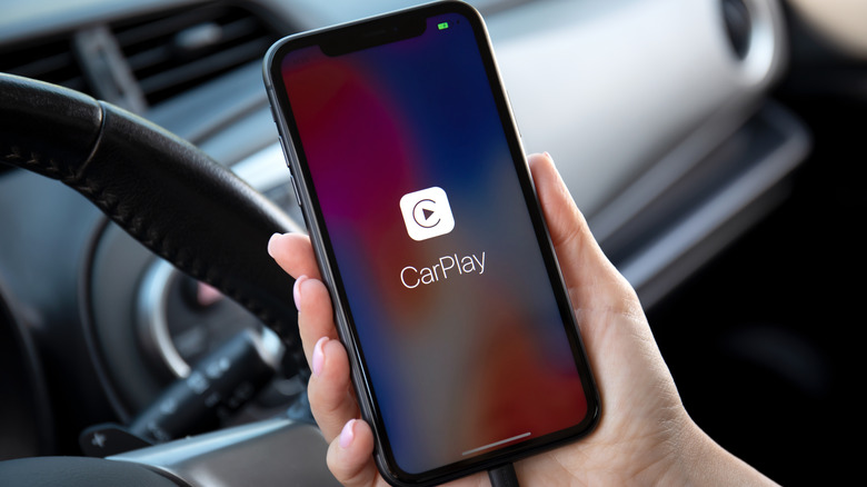 A close-up shot of an iPhone in a car cockpit with the CarPlay logo displayed on the head unit screen.