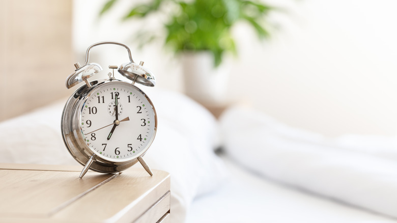 An analog alarm clock resting on a minimalist nightstand in a softly lit room.
